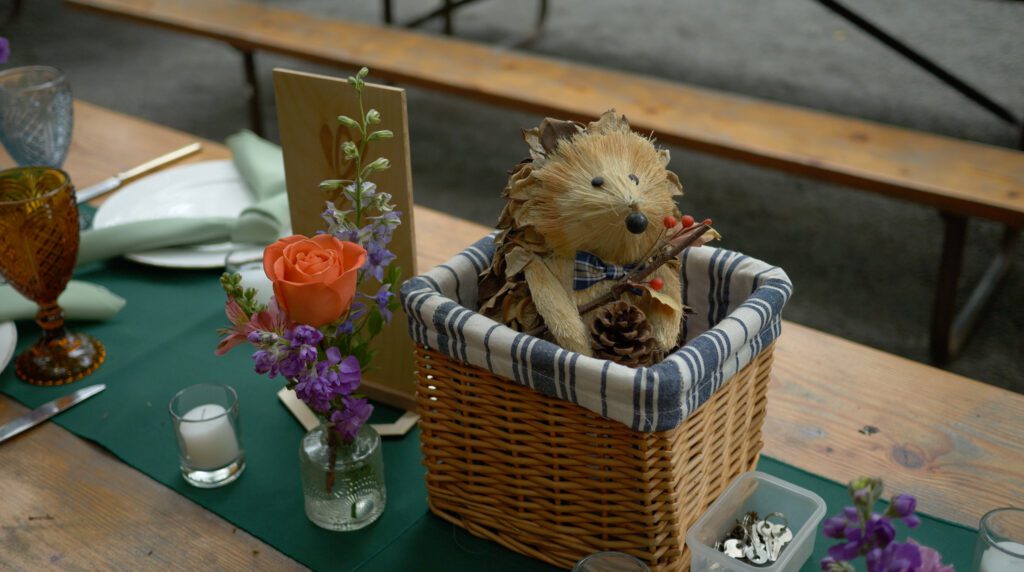 A cute hedgehog made from straw and pinecones sits wearing a bowtie in a little whicker basket.